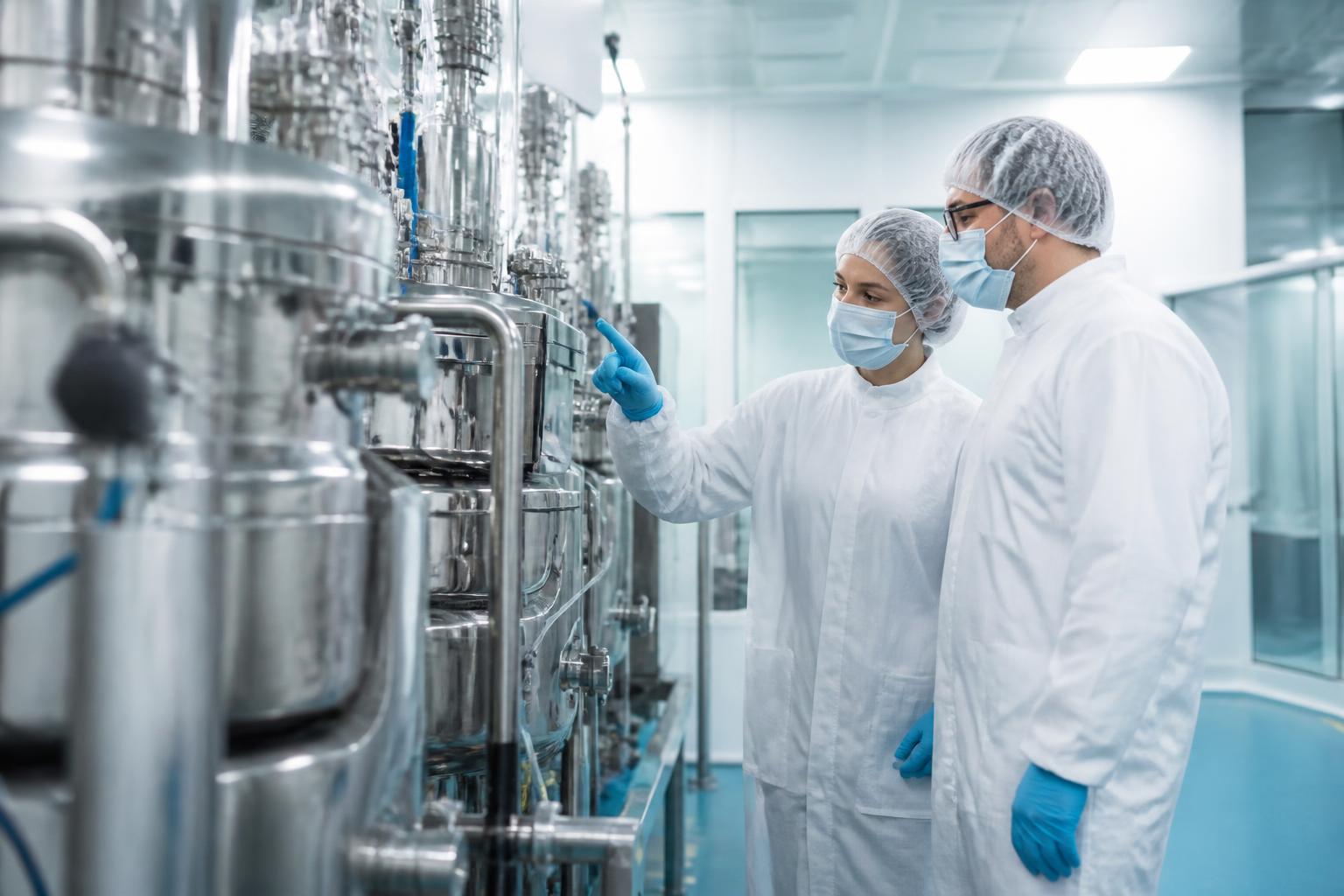 Operators in clean-room gowning reviewing production data on a screen beside sterile filling equipment.